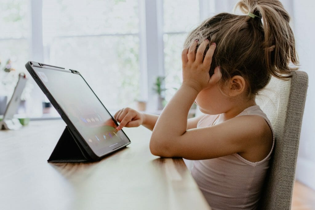 Niña tocando con su dedo una tablet mientras se toca la cabeza