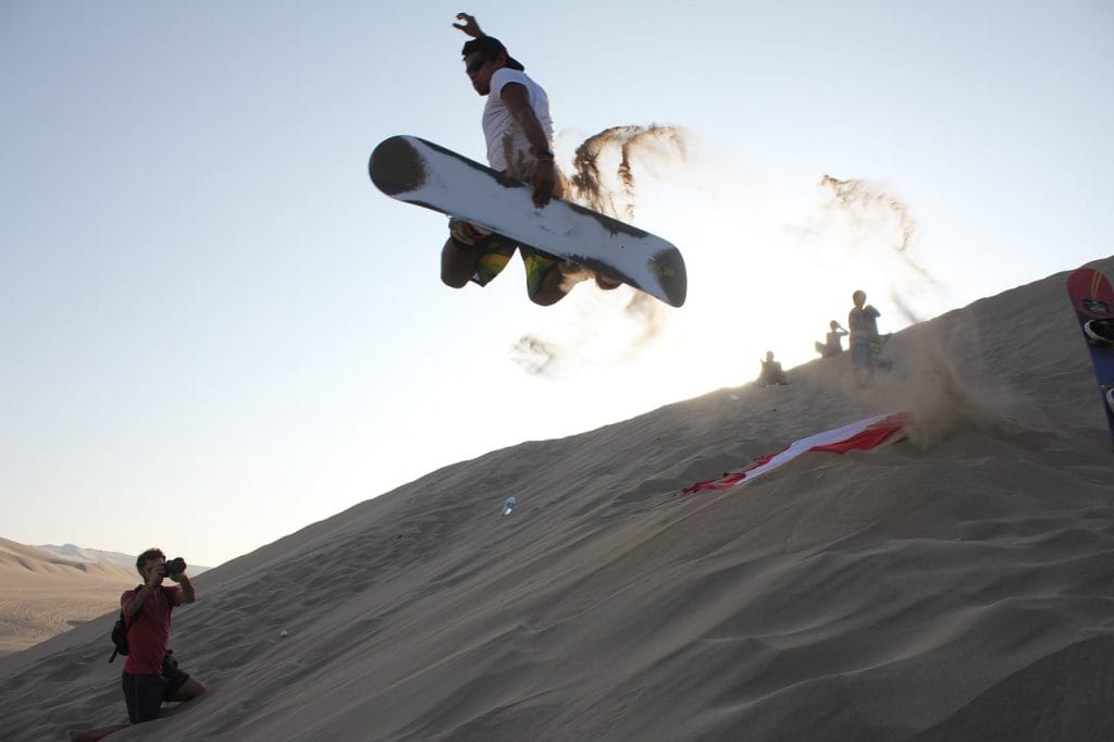 Persona saltando con tabla sobre dunas en oasis Huacachina